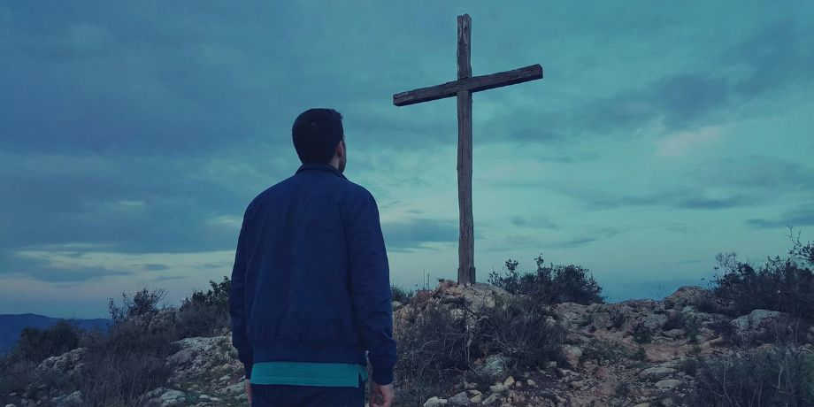 صورة تحتوي على رجل ينظر إلى صليب