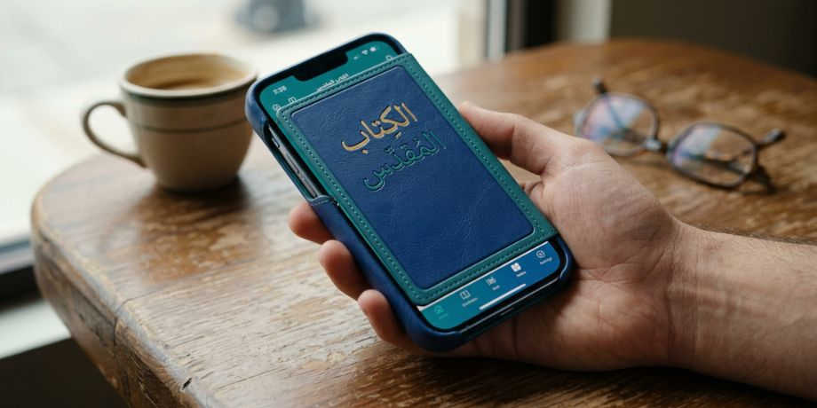 صورة تحتوي على شخص يقرأ الإنجيل من خلال الهاتف المحمول